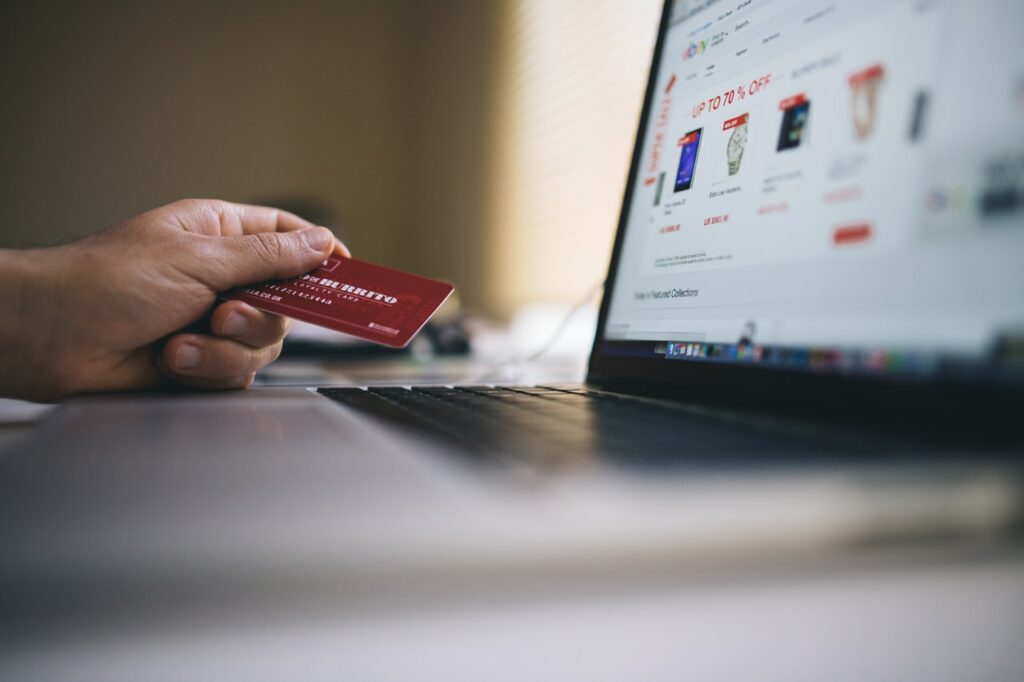 Mão segurando um cartão de crédito vermelho em frente ao computador.