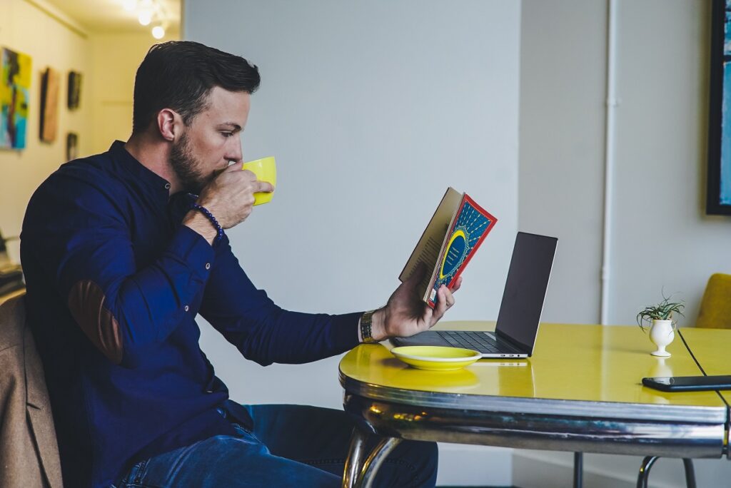 Homem tomando café e praticando o hábito da leitura.